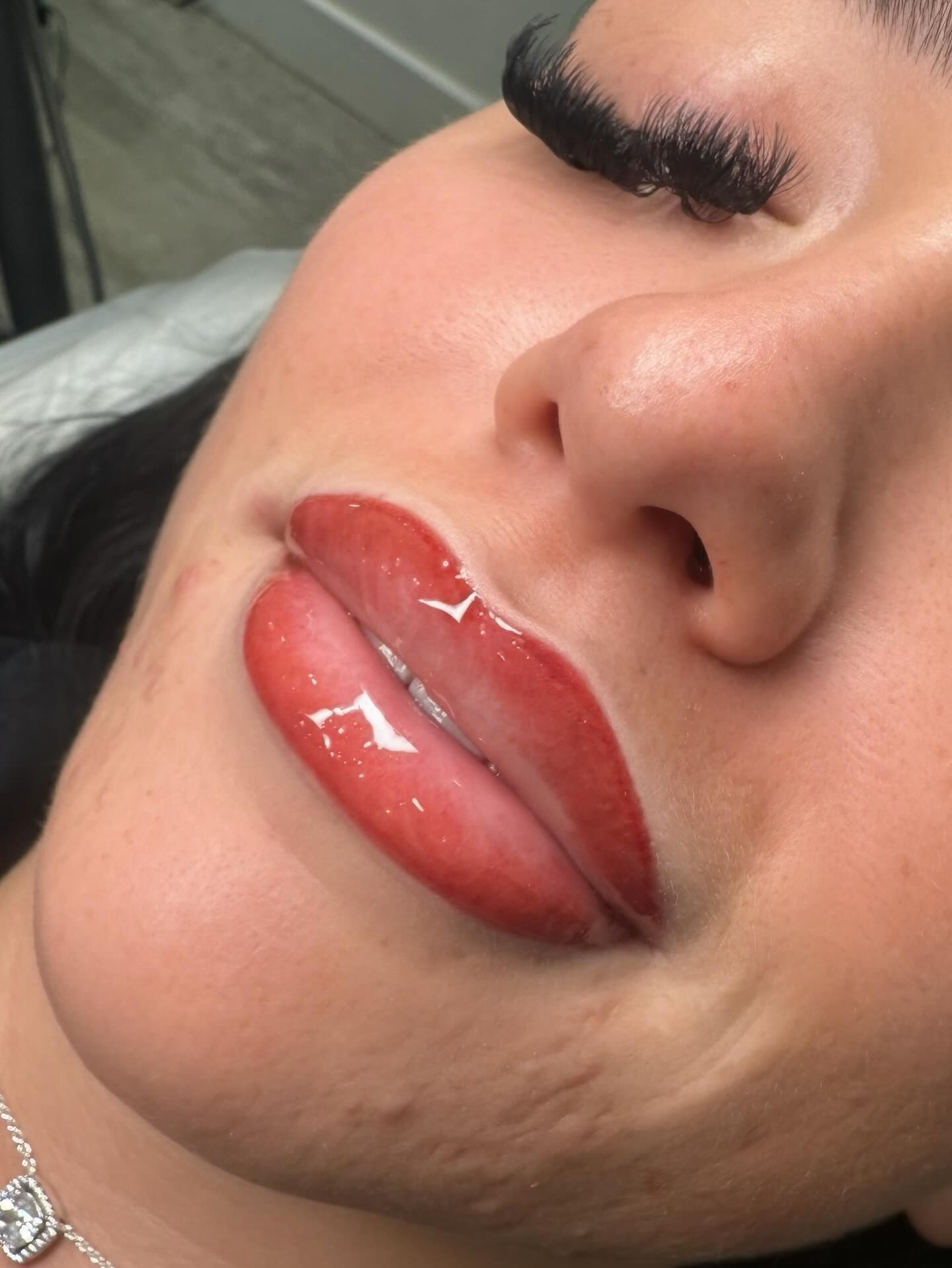 Close-up of lips with red lip color and glossy finish. Person's face is visible with closed eyes.