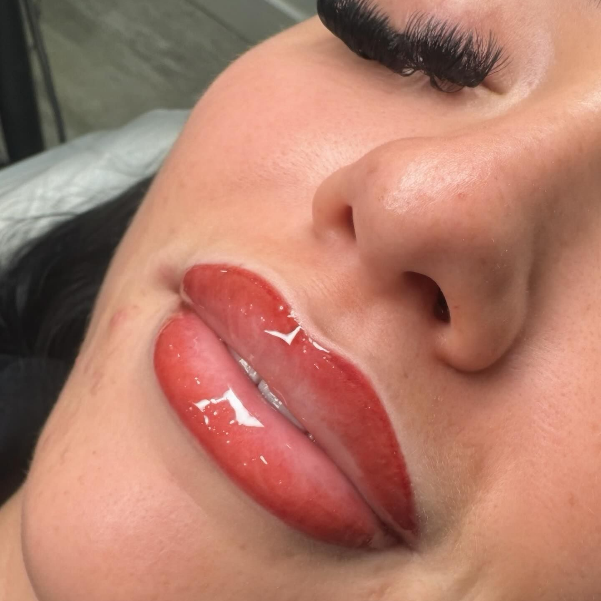 Close-up of lips with red lip color and glossy finish. Person's face is visible with closed eyes.