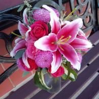 Pink and white lilies with roses in a hanging flower arrangement on a wrought-iron balcony */}