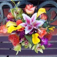 Colorful bouquet of lilies and mixed flowers in a hanging planter against a dark railing