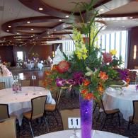 Floral centerpiece with purple vase on a banquet table in a decorated dining room