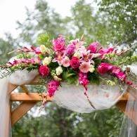 Floral arrangement of pink and white flowers draped over a wooden outdoor arch against trees