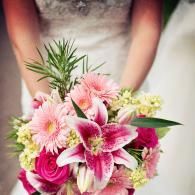 Bouquet of pink lilies, roses, and daisies held by someone in a wedding dress