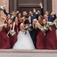 Wedding party posing on steps, bride in white surrounded by attendants in burgundy dresses and dark suits