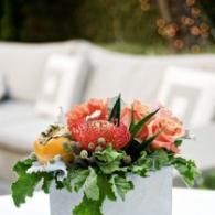 Colorful floral centerpiece with orange and pink blooms in a white vase on a table outdoors