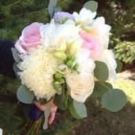 Pastel pink, white, and green bridal bouquet held outdoors against a grassy background