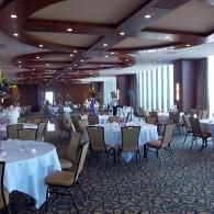 Empty banquet hall with round tables, beige chairs, and patterned carpet under a curved ceiling.