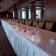 Long banquet table with white tablecloth, beige chairs, and small candle centerpieces in a hotel ballroom