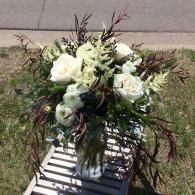 White floral bouquet in a clear vase on a striped outdoor bench, with greenery and dark branches