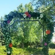 Floral arch covered in green vines and colorful flowers in a sunny garden setting