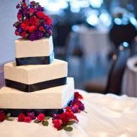 Three-tier white cake with black ribbon and red-purple flowers on a table