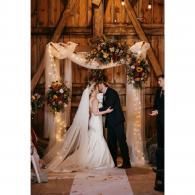Bride and groom kissing beneath a floral arch in a rustic barn wedding venue