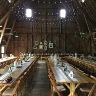 Rustic barn-style hall with long wooden tables and benches arranged for a large gathering