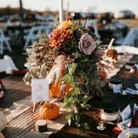 Fall table centerpiece with pumpkins, flowers, candles, and place settings outdoors