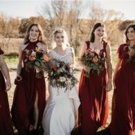 Bride and bridesmaids in burgundy dresses holding bouquets outdoors in autumn light
