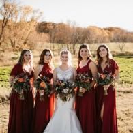 Bride with four bridesmaids in burgundy dresses holding bouquets outdoors