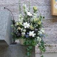 White floral arrangement with greenery on a stone ledge beside a brick wall