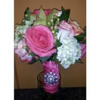 Pink and white floral bouquet in a glass vase with a pink ribbon on a table