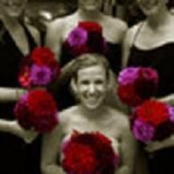 Smiling cheerleader in a black-and-red uniform holding red pom-poms with teammates behind her