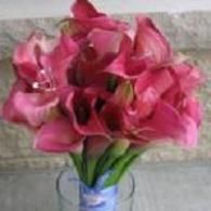 Pink calla lilies in a glass vase against a stone wall