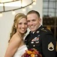 Smiling couple posing at a wedding, bride holding a colorful bouquet and groom in dress uniform.