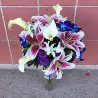 Bouquet of pink, white, and purple lilies in a glass vase on a concrete surface against a tiled wall