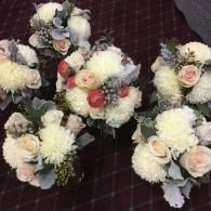 Three small bouquets of white and pale pink flowers with dark greenery on a burgundy checkered cloth