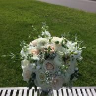 White floral arrangement in a silver vase on grass, with pale roses and greenery.