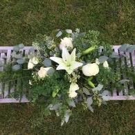 White floral arrangement with lilies and roses on a bench outdoors on grass
