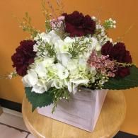 White and burgundy flower arrangement in a translucent square vase on a round wooden table