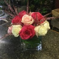 Red, pink, and white roses in a glass vase on a dark countertop.