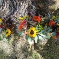 Bouquet of yellow and orange flowers on grass beside a tree trunk