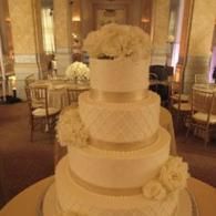 Four-tier white wedding cake with floral topper in an elegant ballroom