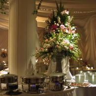 Elegant banquet table with a tall white-and-pink floral centerpiece in a softly lit draped room