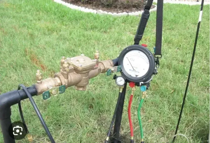 Water meter assembly with a pressure gauge and black pipes on a lawn. Water meter assembly with a pressure gauge and black pipes on a lawn.