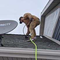 A man is working on the roof of a house with a hose.