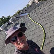 A man wearing a hat and sunglasses is standing on top of a roof.