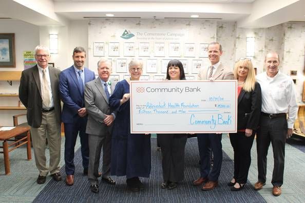 Group of nine people holding a large check from Community Bank.