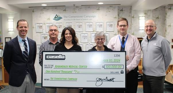 Six people pose behind a large check. They stand in front of a wall with framed items.