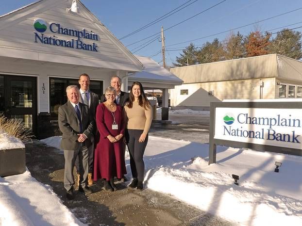 Five people stand in front of a Champlain National Bank branch on a snowy day. The sign has the bank's logo.