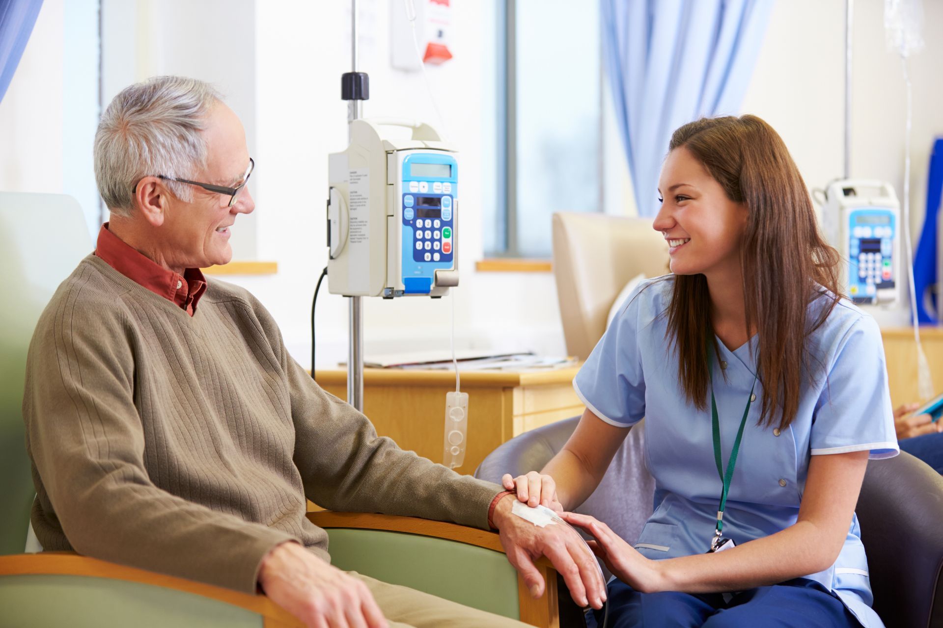 Elderly man receiving IV treatment, smiling with nurse in a hospital room.