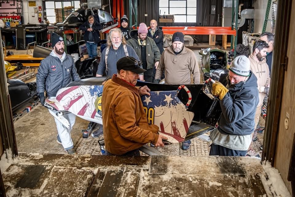 A group of people carrying a decorated casket out a doorway. The casket is painted with an American flag motif.
