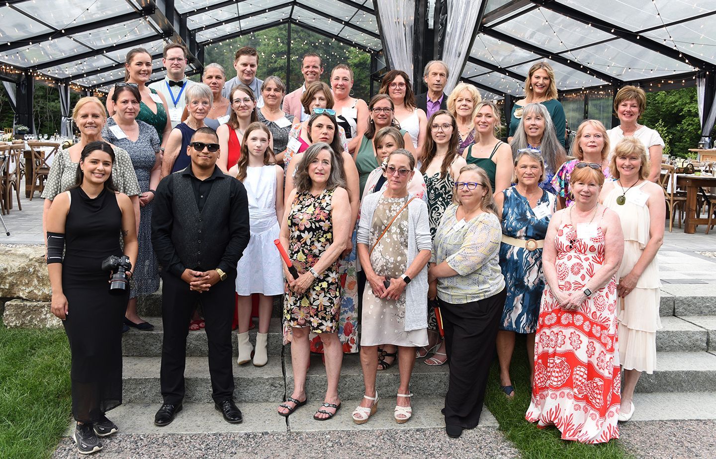 Group photo of approximately 40 people of various ages and ethnicities standing on stone steps in front of a glass structure.