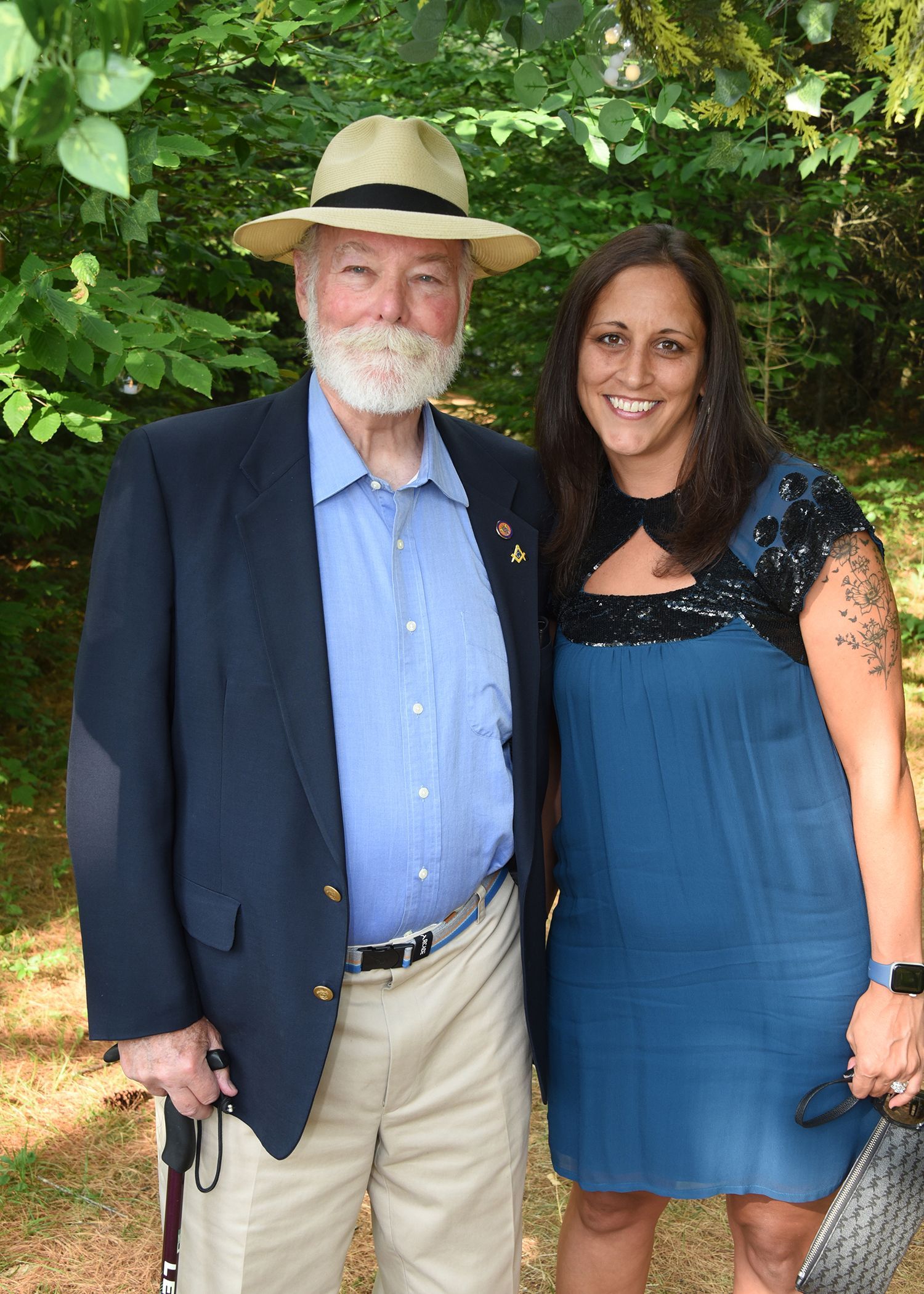 An older man with a white beard and straw hat stands next to a younger woman. 