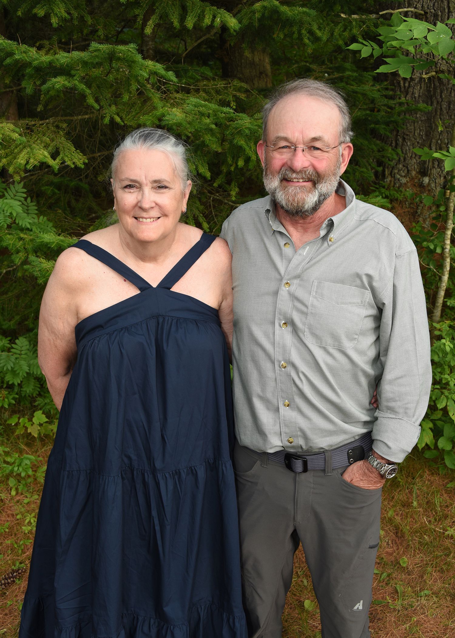An older couple stands side-by-side outdoors, smiling.