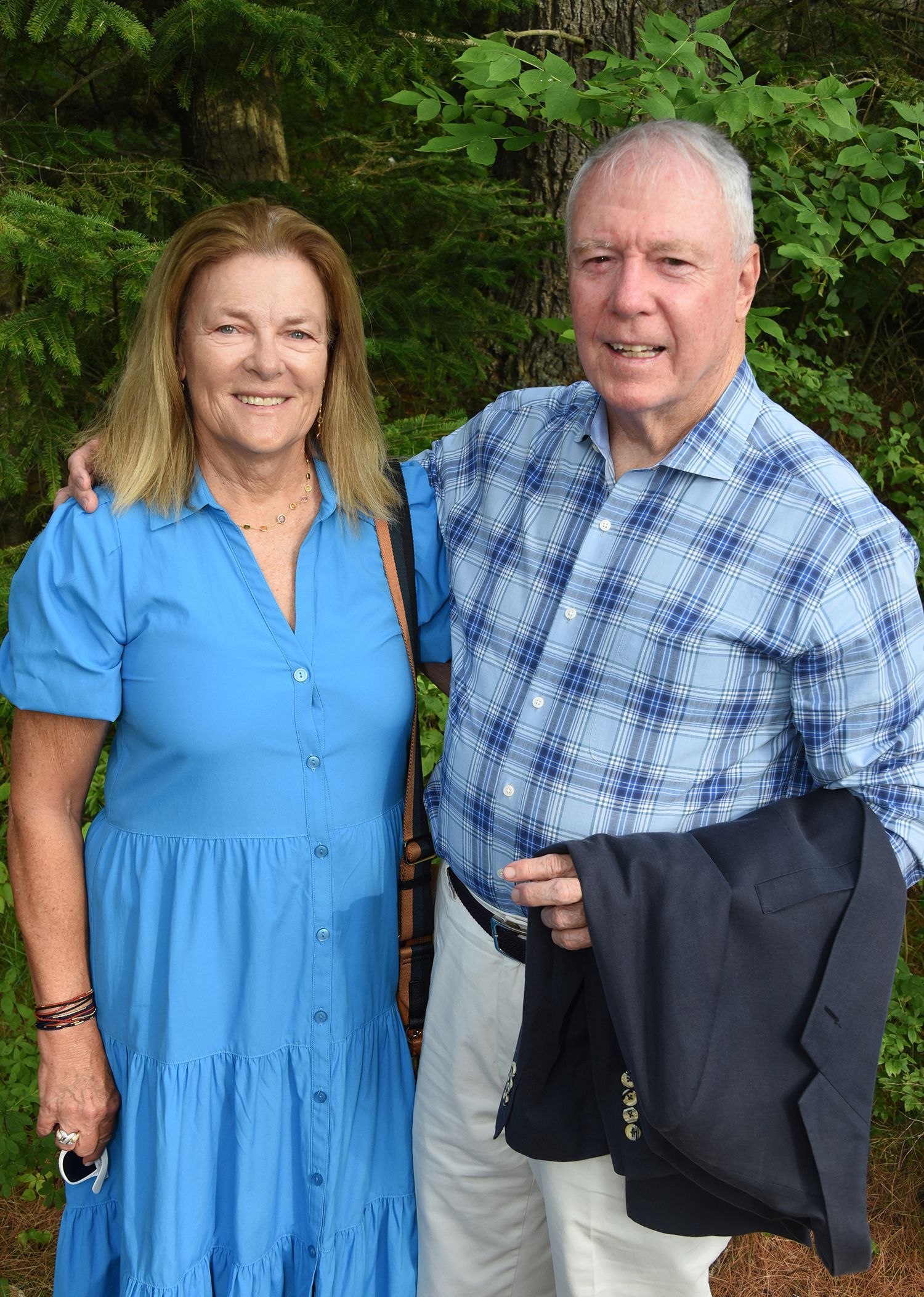 An older couple stands outdoors. The woman wears a blue dress and smiles. 
