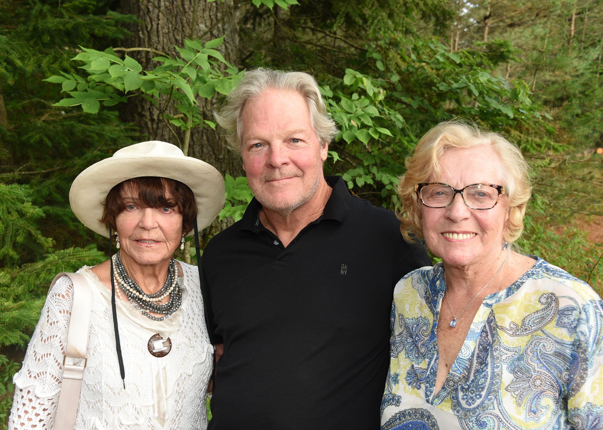 Three people, two women and a man, smiling outdoors. The man stands between the women.