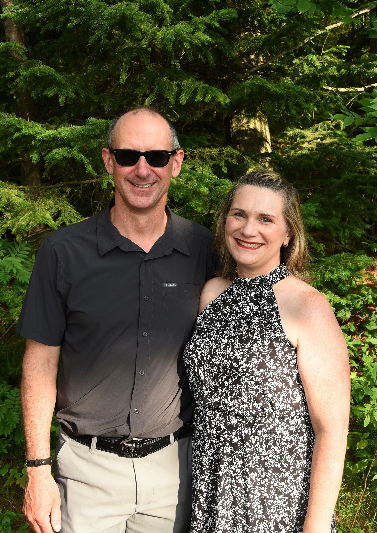 A smiling man and woman standing in front of green foliage. 
