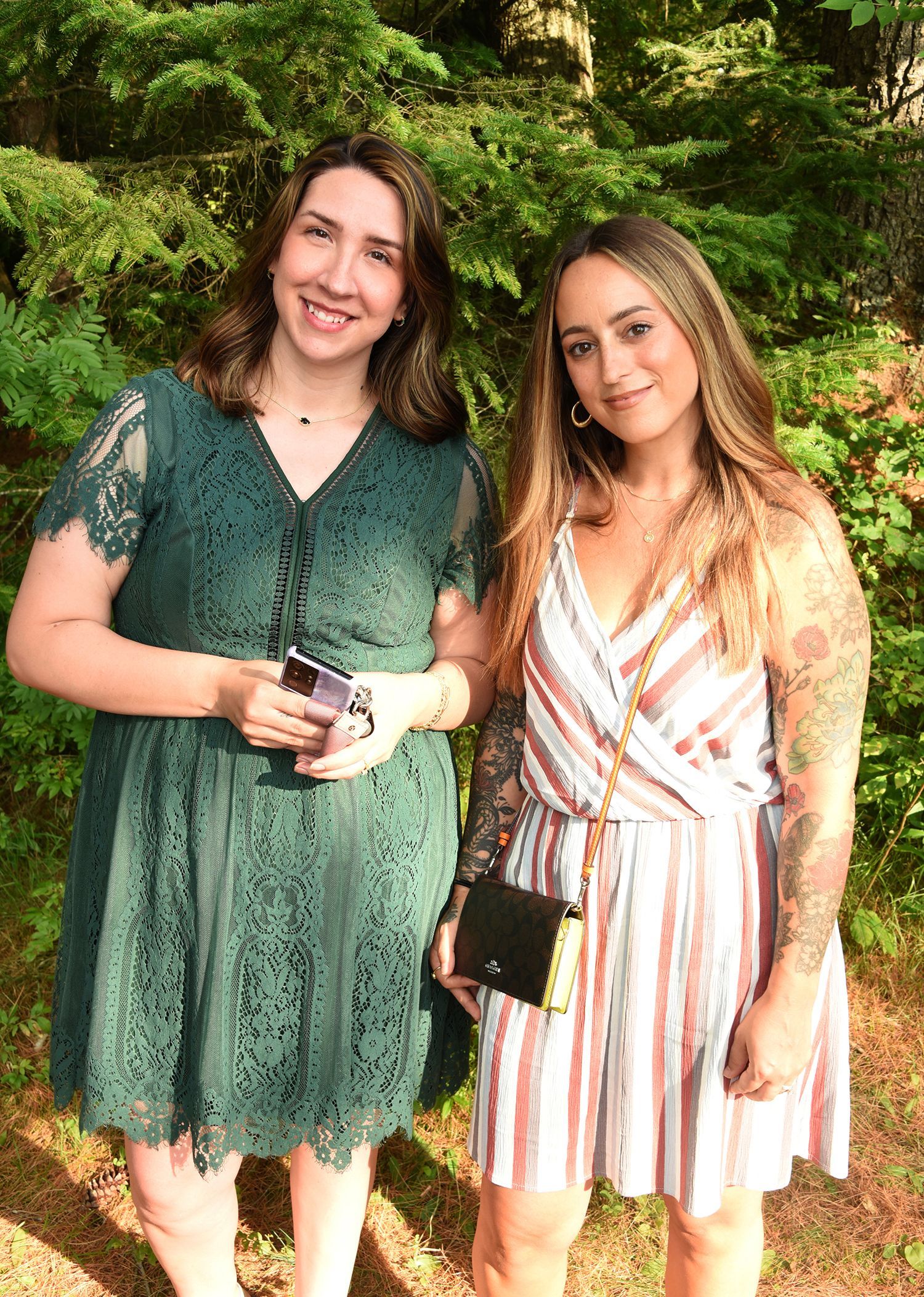 Two women smiling outside. One wears a green lace dress, the other a striped romper.