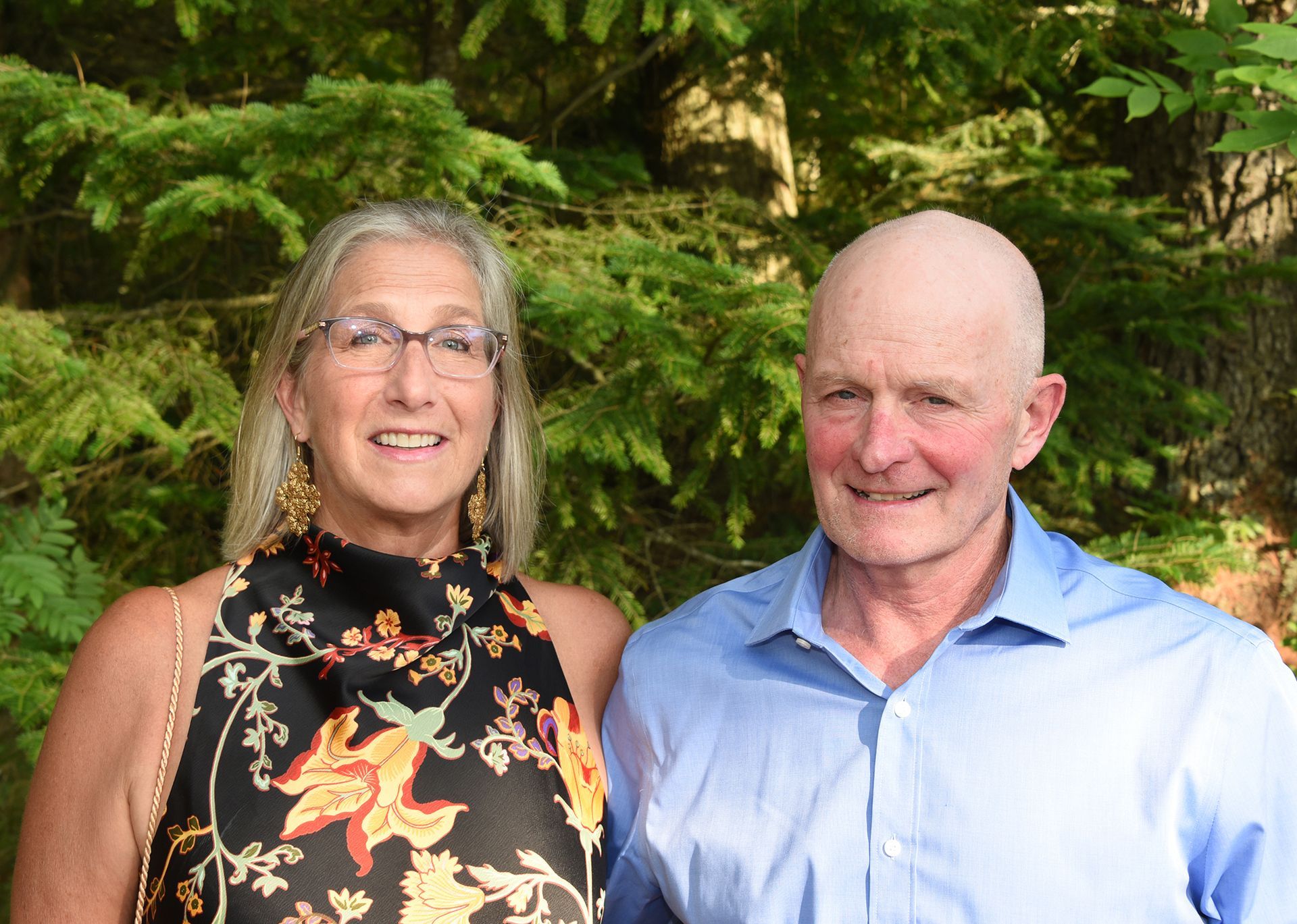 A woman and a man standing together in front of a green leafy background.